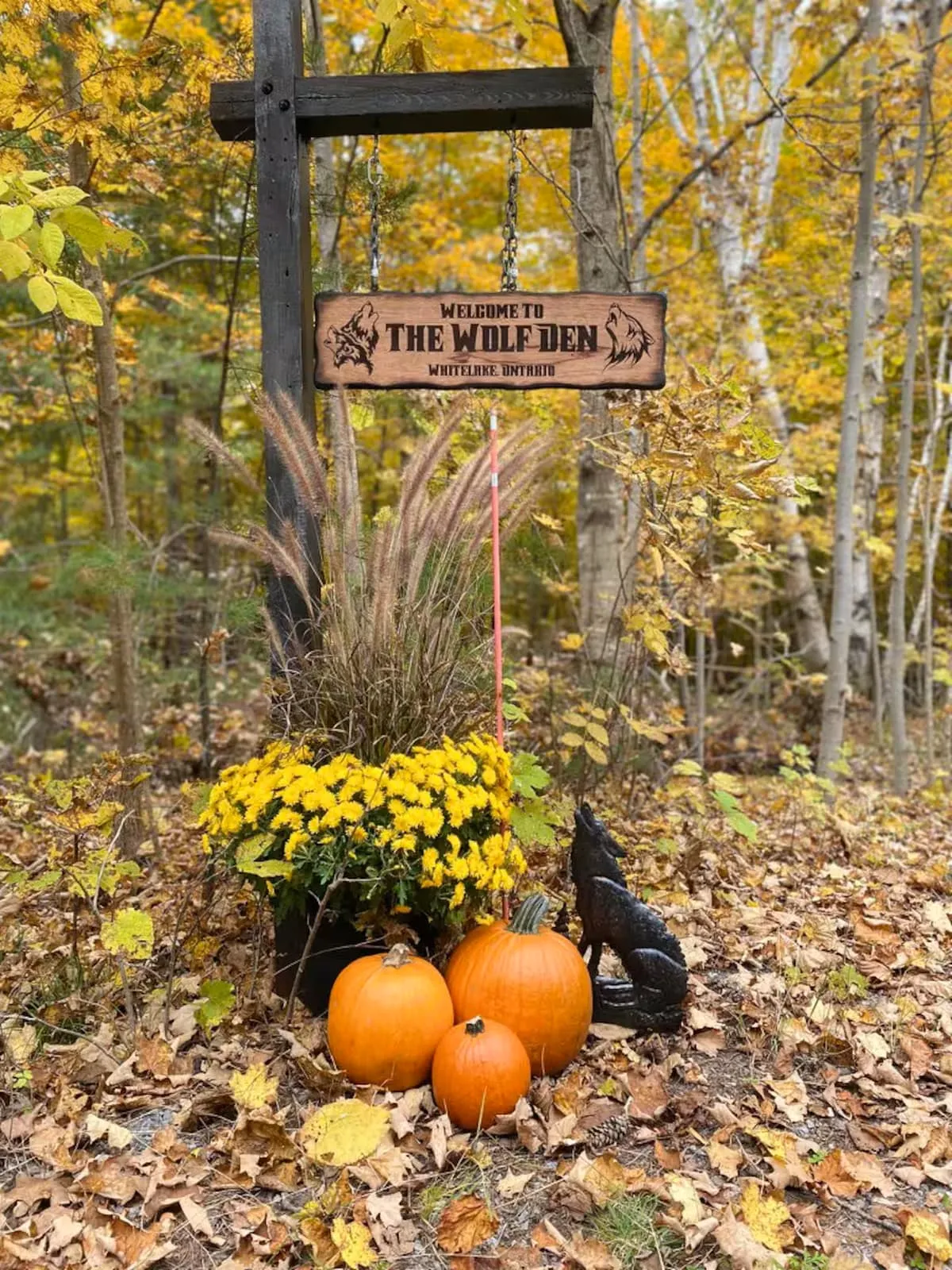The carved Welcome to The Wolf Den sign at the driveway entrance, surrounded by autumn leaves